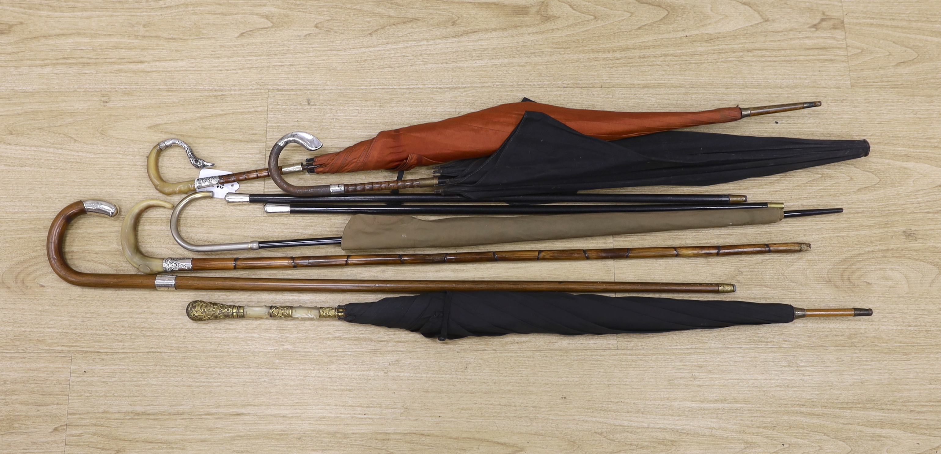 Various vintage umbrellas and walking sticks, three with silver mounted handles and two ebonised swagger sticks with silver tops